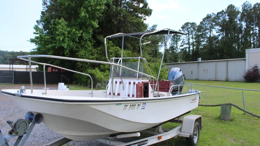 1982 Boston Whaler 17 Montauk center console boat on trailer with Yamaha 90hp outboard engine, surrounded by greenery and a storage building in the background.