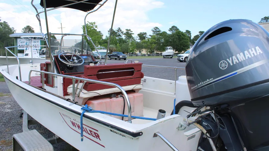 1982 Boston Whaler 17 Montauk center console boat with Yamaha 90hp outboard engine, featuring a steering wheel, red seating, and storage compartments, showcased in a marine setting.
