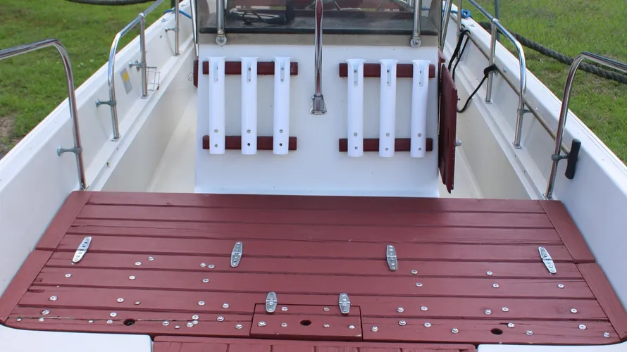 Interior view of a 1982 Boston Whaler 17 Montauk featuring a spacious deck with red wood flooring, white rod holders, and a clean, well-maintained center console layout, emphasizing its classic design and functionality for boating enthusiasts.