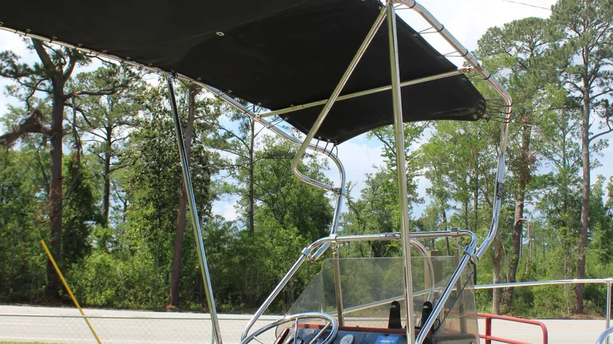 1982 Boston Whaler 17 Montauk center console boat with a black bimini top, showcasing a dashboard and seating area, set against a backdrop of trees.