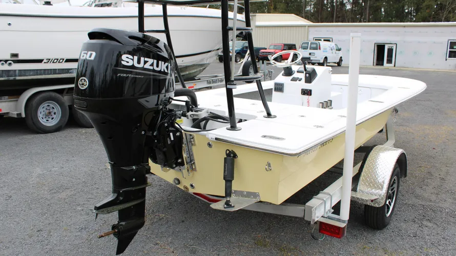 2025 Mitzi Skiff 17 Tournament in Fighting Lady Yellow with a 60hp Suzuki outboard motor, showcasing boat features including live wells and a trailer, set against a backdrop of vehicles and a service building.