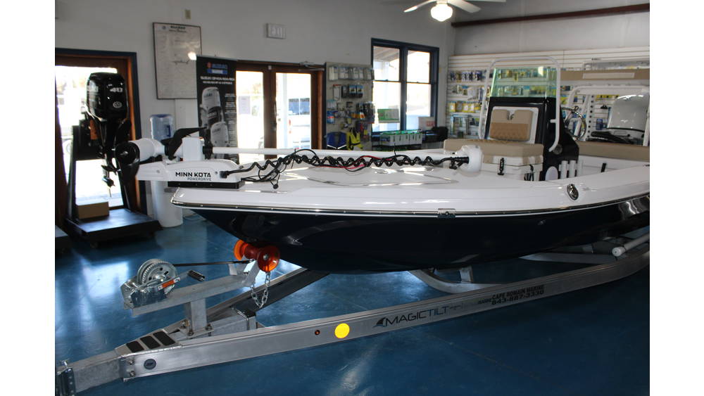 2025 Action Craft 17 Flyfisher boat displayed indoors, featuring a Suzuki outboard motor, Minn Kota trolling motor, and a bunk trailer, set against a backdrop of marine accessories and equipment.