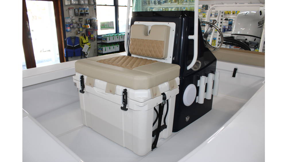 Interior view of the 2025 Action Craft 17 Flyfisher boat showcasing a beige cushioned seat and storage compartment, with a sleek black console and visible Suzuki outboard motor in the background, highlighting features for potential buyers at Cape Romain Marine.