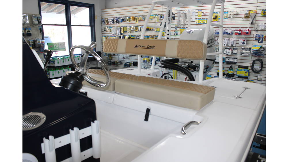 Interior view of a 2025 Action Craft 17 Flyfisher boat featuring a steering wheel, beige cushioned seating, and Suzuki outboard motor, set against a backdrop of marine accessories.