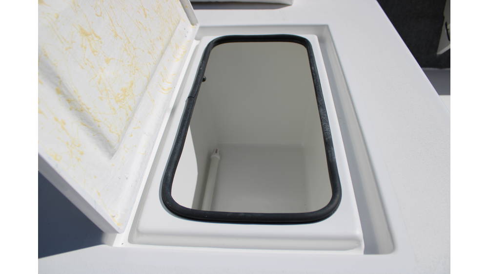 Interior view of a storage compartment with a lid, featuring a clean, white finish, designed for the 2025 17 Tournament Mitzi Skiff, highlighting its practical features for boat storage.