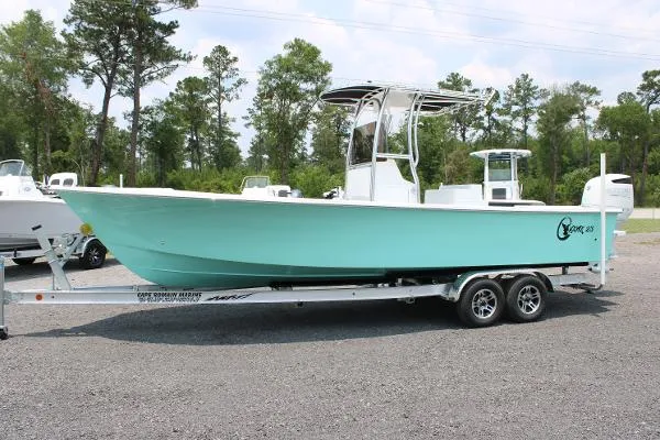 2025 C-Hawk 25 Center Console boat in Seamist color, showcasing a dual-axle trailer, positioned outdoors among trees, ideal for saltwater fishing and family boating.